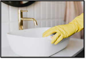 A gloved hand cleaning the bathroom sink